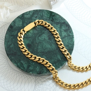 Collier à grosse chaîne gourmette dorée sur socle en marbre vert avec décor floral