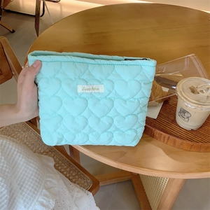 Mint green heart quilted cosmetic bag on a wooden table with coffee and croissants