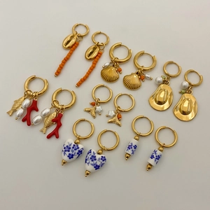 Golden earrings set with blue ceramic, seashell, and starfish charms on white background