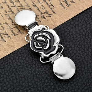 Detail of vintage silver shawl clip featuring a black rose motif on a rustic background