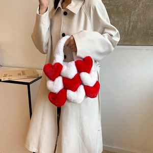 Close-up of heart-shaped plush tote bag in red and white faux fur held by model