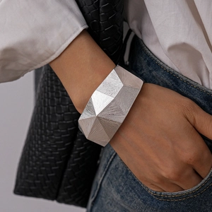Detailaufnahme einer breiten silbernen Manschette mit facettierter Metallstruktur am Handgelenk