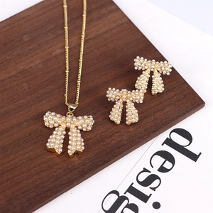 Elegant gold-tone jewelry set featuring pearl-embellished bow necklace and earrings