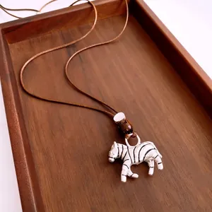 Vintage zebra pendant necklace with brown leather cord and enamel finish in a wood tray