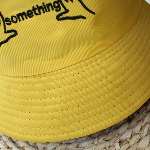 Close-up of yellow cotton bucket hat featuring precise black something embroidery detail