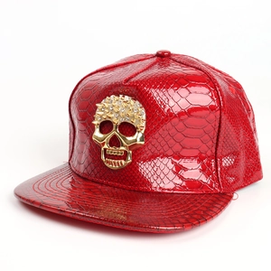 Detail of red faux snakeskin leather cap with a golden skull emblem and metallic studs