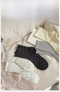 Detail view of five colors of polka dot cotton socks arranged on a soft beige sofa