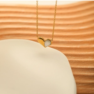 Detailed close-up of a gold heart pendant necklace with white shell inlay on a wooden base