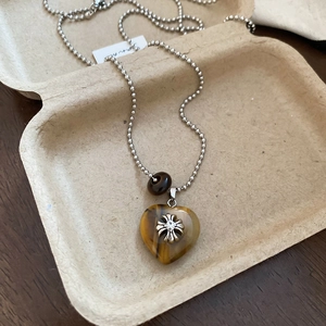 Macro shot of tiger eye stone heart pendant with metal cross on bead chain
