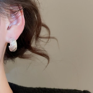 Close-up of silver-tone C-shaped hoop earrings with woven texture on a model