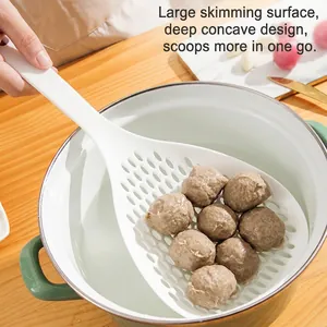 Large white slotted spoon scooping meatballs from a white pot in a bright kitchen setting