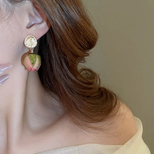 Close-up of golden irregular disk earrings with dried rose bud pendants on a model