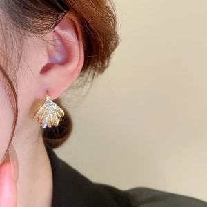 Gros plan d'une boucle d'oreille coquillage dorée avec cristaux sur l'oreille