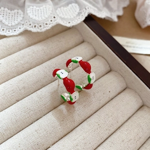Close-up of red and green enamel apple stud earrings on a beige velvet jewelry box
