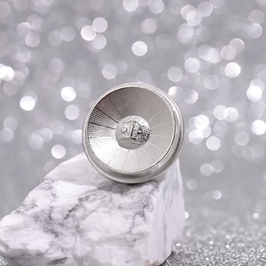 Elegant silver metal brooch pin with circular textured pattern on white marble stone