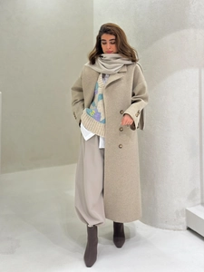 Full body shot of a beige wool coat styled with a matching scarf and knit vest