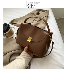 Detail view of coffee brown faux leather handbag with gold lock and top handle