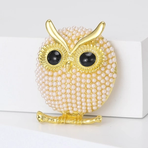 Close-up of golden owl brooch with white imitation pearls and black crystal eyes