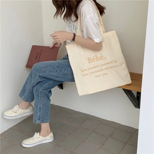 Detail der cremefarbenen Canvas-Tasche mit braunem Zitat-Stickmuster von Person in weißem T-Shirt