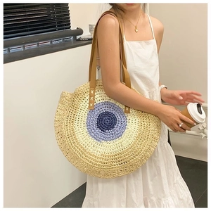 Detail view of large circular straw beach bag with navy and purple patchwork pattern