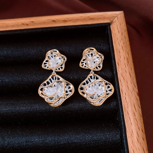 Detailed close-up of hollow layered flower earrings in gold and silver on black velvet