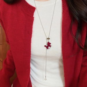 Détail d'un collier pendentif poney rouge avec cristaux et perle sur un pull rouge
