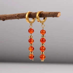 Vintage stainless steel earrings with orange bead pendants hanging on a wood branch