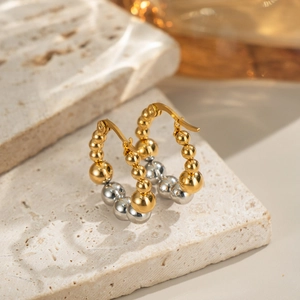 Macro shot of two-tone beaded hoop earrings in gold and silver on a textured stone