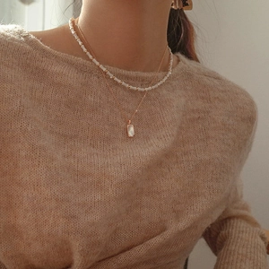 Close-up of a layered gold necklace with shell pendant on a beige knit sweater