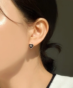 Detailed view of silver heart earring with black enamel and small bow on model ear