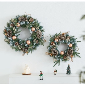 Detail of frosted Christmas wreath with pine cones and gold ornaments on white wall