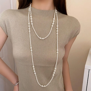 Dettaglio di una collana di perle irregolari a più strati su un maglione beige