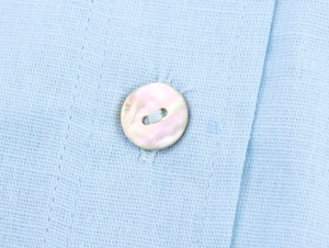 Macro view of blue linen fabric texture and iridescent shell buttons on a casual shirt
