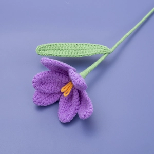 Close-up of handmade purple knitted tulip flower with yellow stamen and green leaf