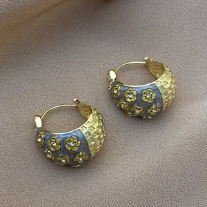 Detailed close-up of vintage flower hoop earrings with zircon on champagne silk background
