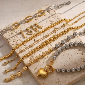 Minimalist gold and silver beaded bracelets with LOVE letter charms on stone background