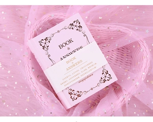 Close-up of pink Book of Answers notebook with gold foil patterns in a dreamy basket