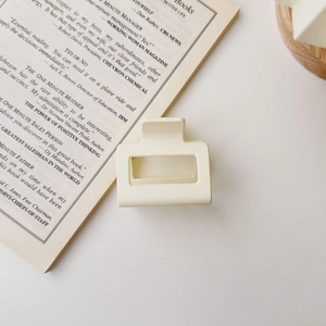 Detailed close-up of a matte cream square hair claw clip on a minimalist book background