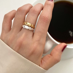 Close-up of gold and silver twisted croissant rings layered on model's finger