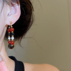 Detailed close-up of vintage beaded drop earrings with red, black and pearl beads on a model