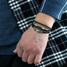 Close-up of multilayer black leather bracelet with metal tubes and feather charm on wrist