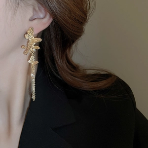 Detailed close-up of golden butterfly fringe earrings with crystals on a female model