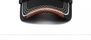 Close-up of black cotton baseball cap brim with white stitching and brown leather edge