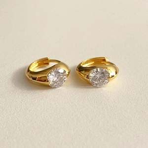 Detailed view of gold hoop earrings with set white zircon on beige background