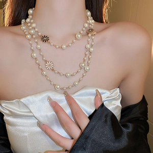 Close-up of layered pearl necklace with golden chains and enamel daisy pendants