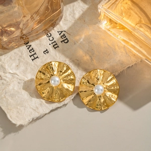 Vintage gold hammered metal drop earrings with pearl detail on a decorative paper