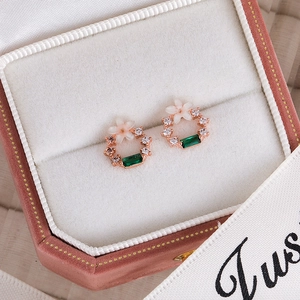 Detailed macro view of a rose gold floral earring with green zircon in a velvet box