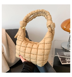 Detail of apricot quilted hobo bag with knotted handle and gold zipper on a sofa