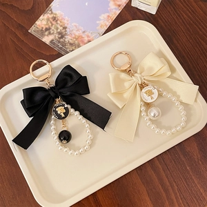 Elegant bow keychain with pearls and metal emblem in black and cream satin finish