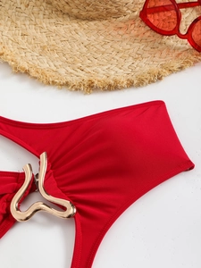 Detail of red swimsuit with wavy golden ring buckle next to straw hat and sunglasses